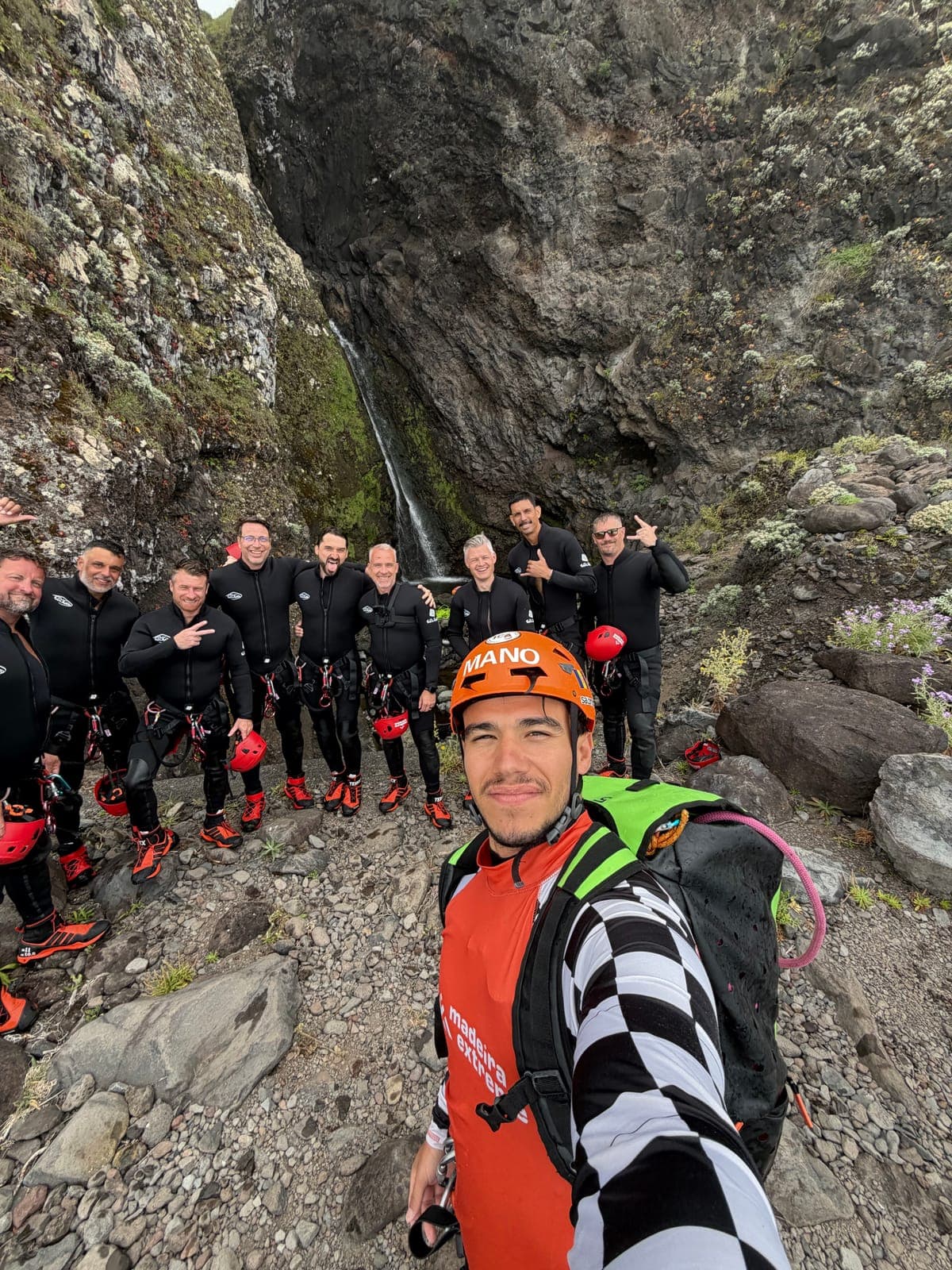 group selfie at a waterfall, orange MANO helmet and madeira extreme vest
