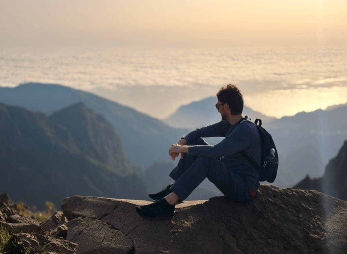 man on a mountain ledge above clouds